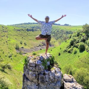 Eric standing in Tree Pose on a rock over Lathkill Dale